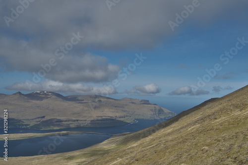 Beautiful perspective scenic view from hiking trail to Sl  ttaratindur to the landscape with eroded mountains in green and ocean in background on a sunny day with dark clouds over the Faroe Islands