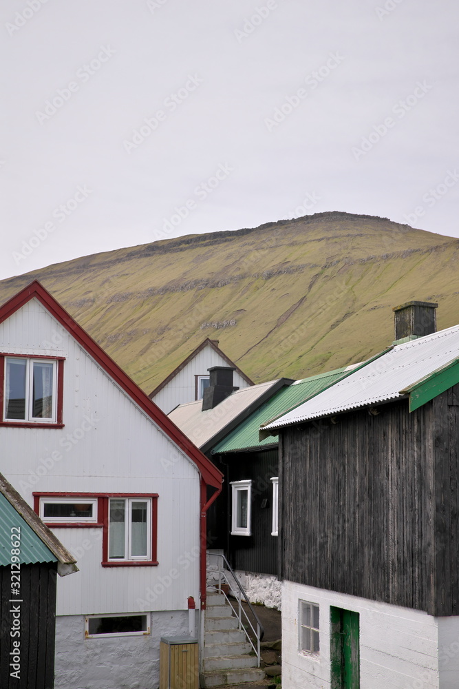 Horizontal scenery image of Faroese landscape with idyllic village Gjogv, most northern village on the island of Eysturoy in foreground and high mountains in background covered with clouds Horizontal scenery image of Faroese landscape with idyllic village Gjogv, most northern village on the island of Eysturoy in foreground and high mountains in background covered with clouds