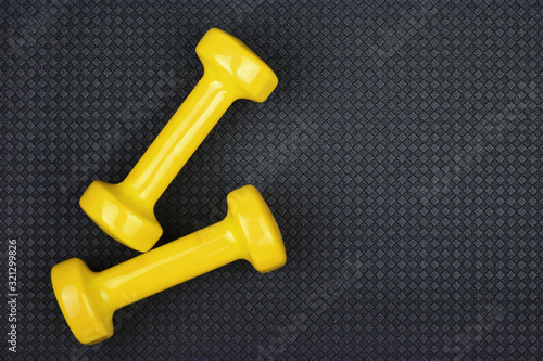 Fitness concept. Weight loss. Yellow dumbbells isolated on grey yoga mat. With copy space for text