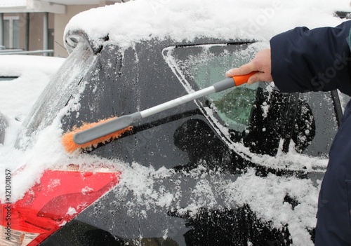 Winter, weather, people and vehicle concept - cleaning snow from car with brush