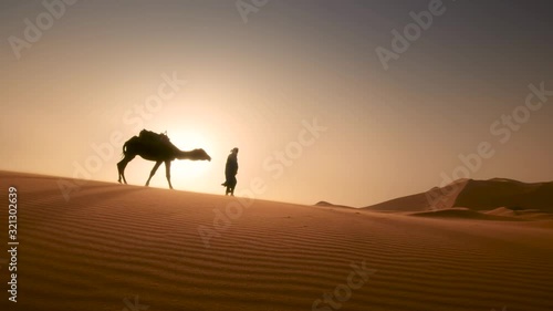 Moroccan cameleers (camel driver) bedouin with camel silhouettes in sand dunes of Merzouas desert. Caravan in Sahara desert travel tourism background safari adventure. Sahara desert of Morocco. photo
