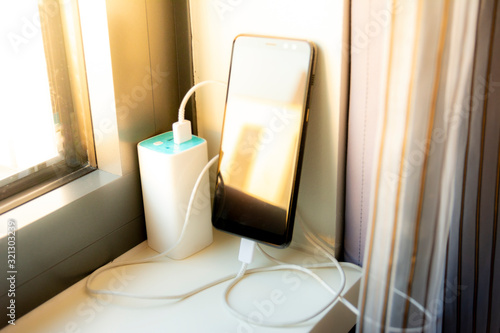 Charging a mobile phone, smartphone, with a battery power bank on the windowsill of a home with sunlight hitting the mobile devices