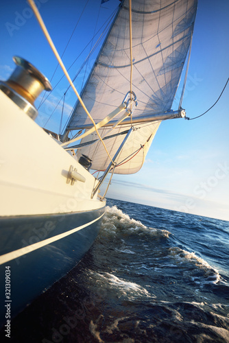 Blue sloop rigged yacht sailing in an open sea on a clear sunny day. Mast and sails lose-up. Waves and water splashes. Baltic sea, Estonia photo