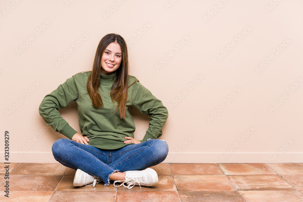 Young caucasian woman sitting on the floor isolated confident keeping hands on hips. Young caucasian woman sitting on the floor isolated confident keeping hands on hips.
