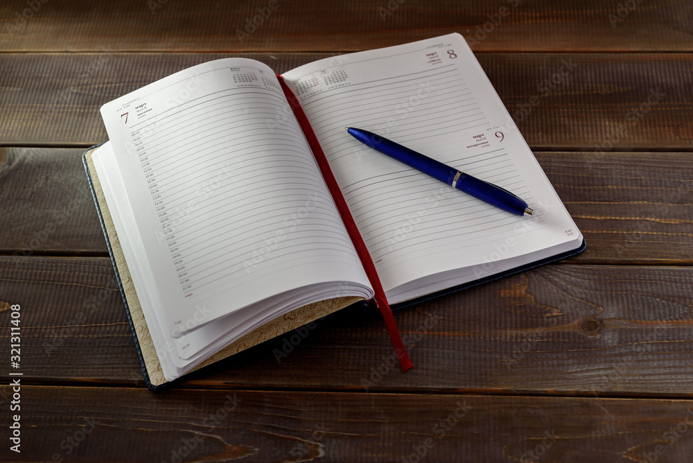 Open note book with pen and books on a wooden table. University exam preparation concept. Open note book with pen and books on a wooden table. University exam preparation concept.