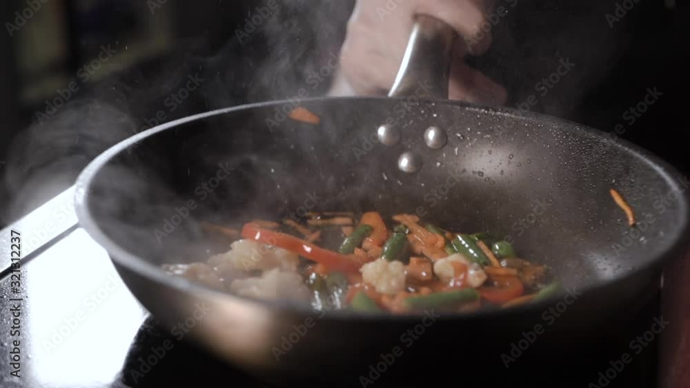 The chef in the kitchen in transparent sterile gloves pours soy sauce from a red bottle of vegetables for wok in a pan, which is fried and stir The chef in the kitchen in transparent sterile gloves pours soy sauce from a red bottle of vegetables for wok in a pan, which is fried and stir
