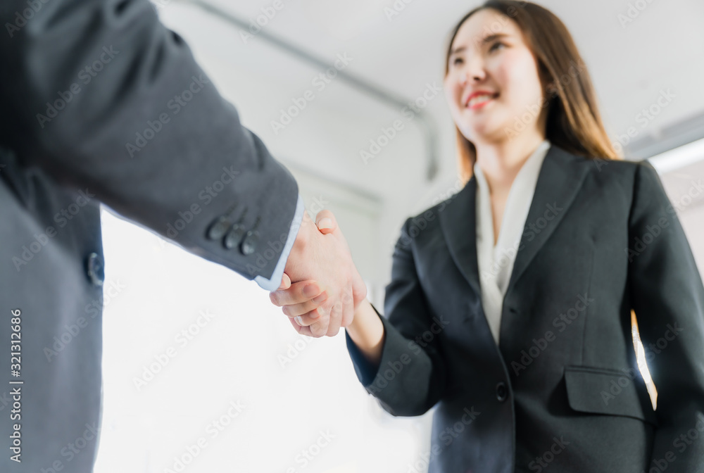 Asian young businesswoman and businessman standing with making handshake after successful about to partnership