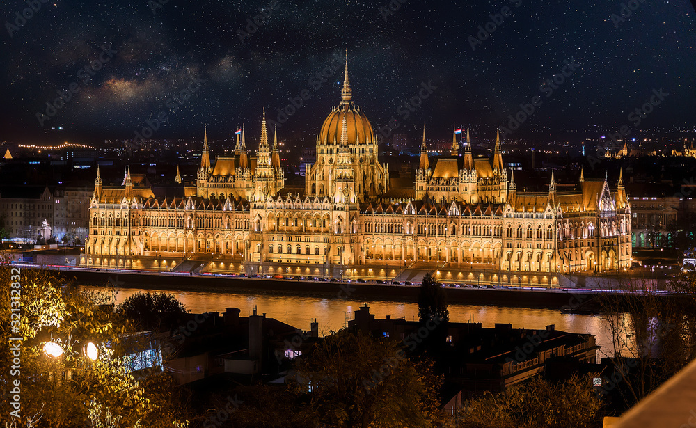 Obraz premium Colorful sunset over Budapest with fantastic sky star and milky way. Night view of the illuminated building of the Hungarian parliament over Danube river with reflected. Popular touristic locations