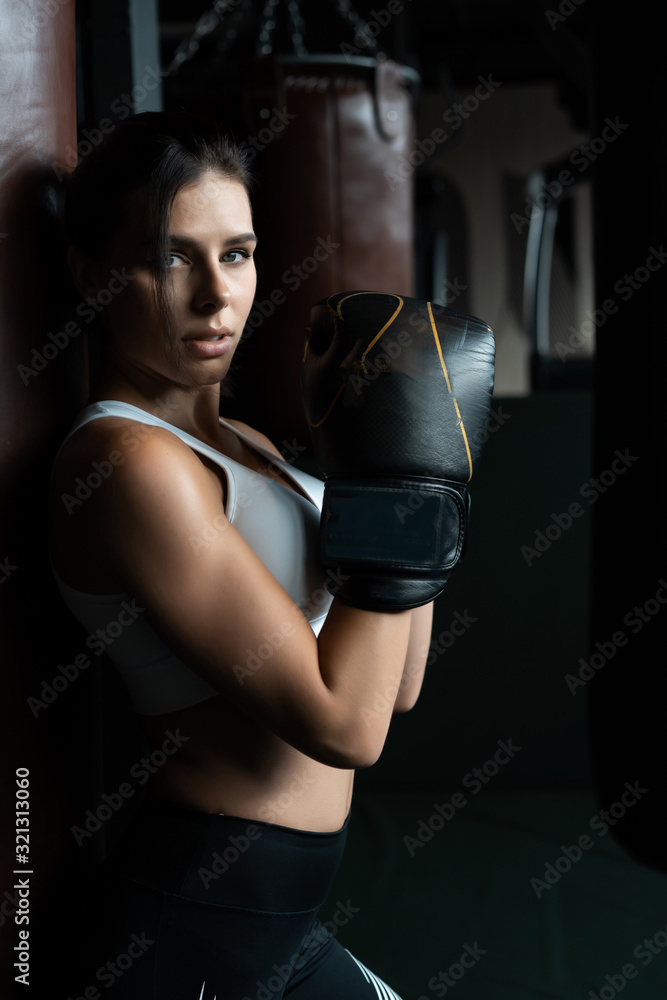 Boxing woman posing with punching bag, on dark background. Strong and independent woman concept