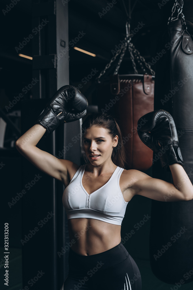 Boxing woman posing with punching bag, on dark background. Strong and independent woman concept
