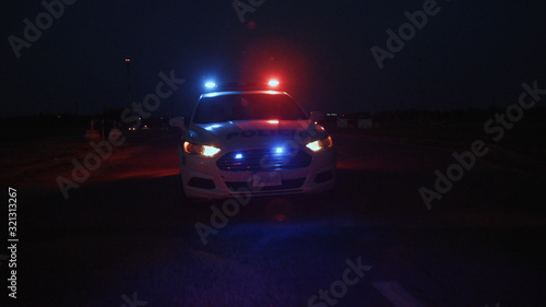 Traffic police car with lights and siren driving high speed along the road against big stadium in the city at night.