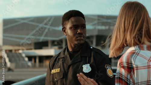 Obraz na plátně Close-up offended young woman talking with afro-american policeman describing the detailes of a car accident