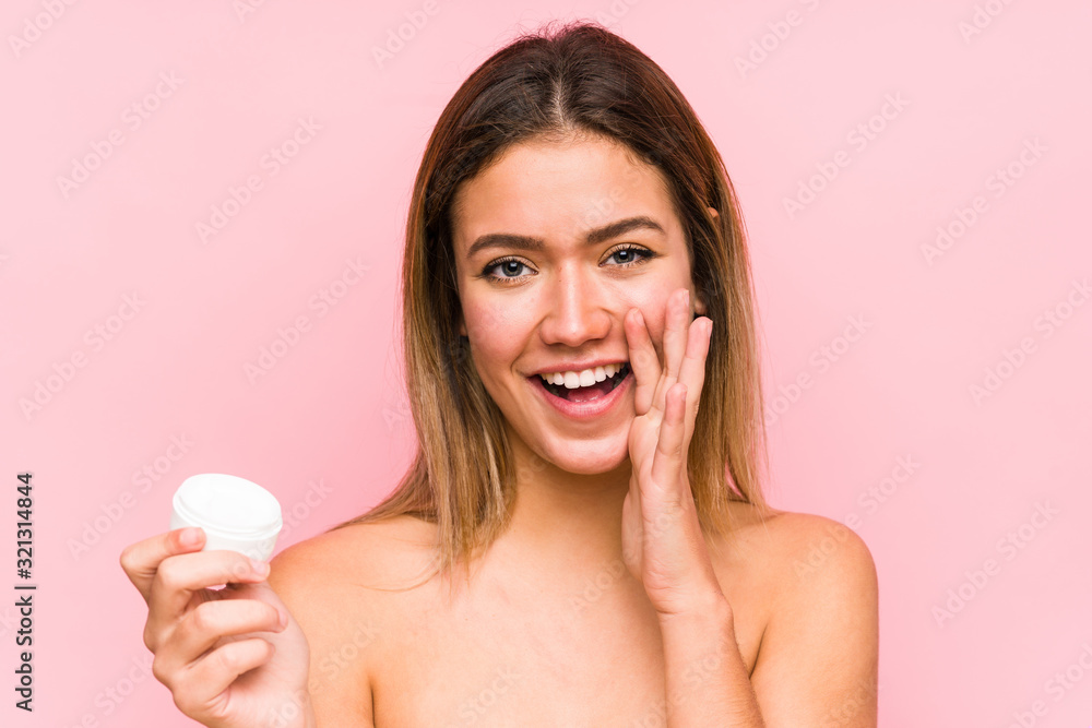 Young caucasian woman holding a moisturizer isolated shouting excited to front. Young caucasian woman holding a moisturizer isolated shouting excited to front.