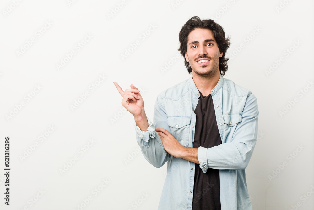 Young handsome man against a white background smiling cheerfully pointing with forefinger away. Young handsome man against a white background smiling cheerfully pointing with forefinger away.