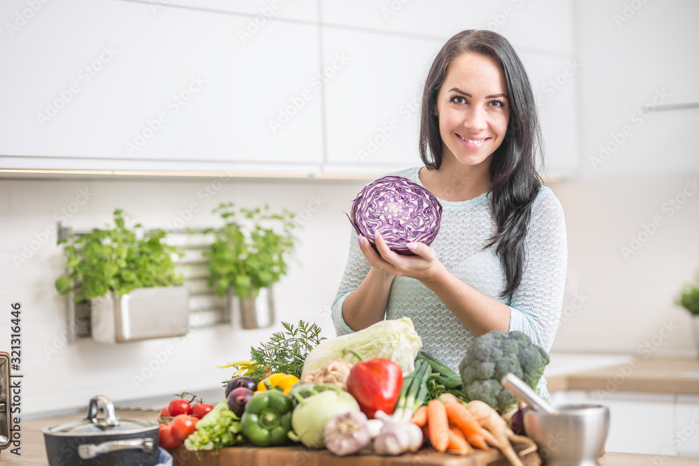 Cheerful young woman with red cabbage and fresh vegetables in her kitchen preparing a healthy lunch Cheerful young woman with red cabbage and fresh vegetables in her kitchen preparing a healthy lunch