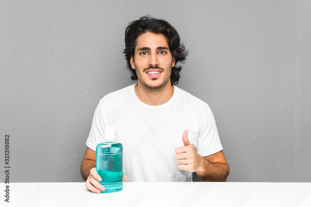Young man holding a mouthwash smiling and raising thumb up Young man holding a mouthwash smiling and raising thumb up
