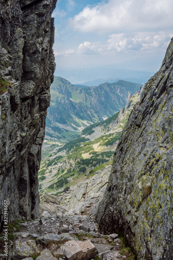 Close up view of a couloir between sharp rocks, behind it reveals a beautiful green valley, Rila mountain, Bulgaria.