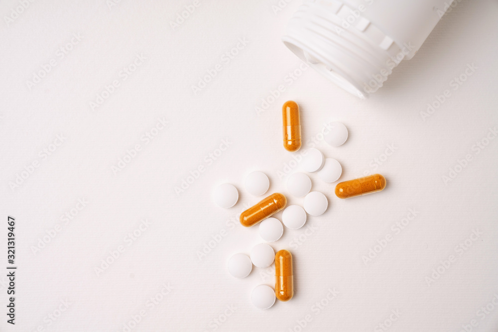 Medical pills and capsules spilled out from white plastic bottle isolated on white background. Top view. Copy space. Medical pills and capsules spilled out from white plastic bottle isolated on white background. Top view. Copy space.