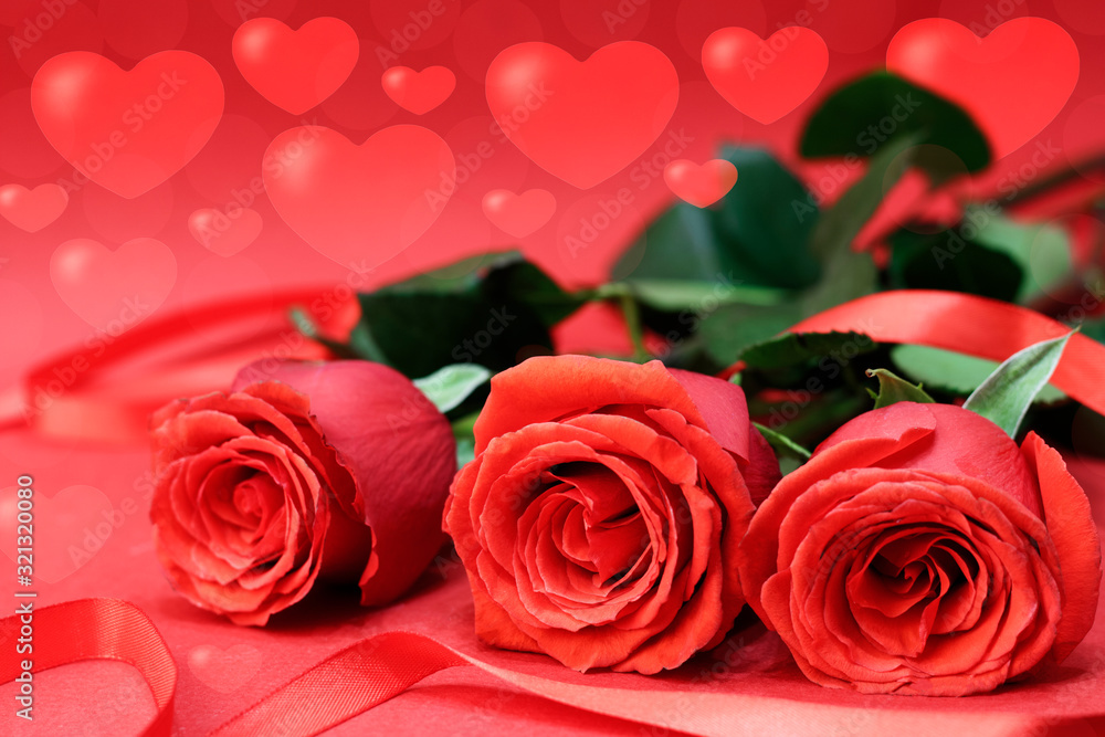 Red roses next to a red ribbon, on a red background with bokeh hearts. Concept card for Valentine's Day. Copy space Red roses next to a red ribbon, on a red background with bokeh hearts. Concept card for Valentine's Day. Copy space