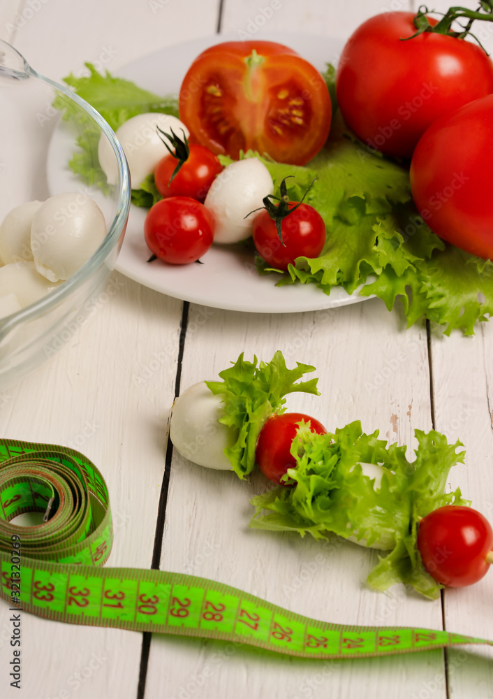 mozzarella cheese, red tomatoes and lettuce on a plate on a light wooden table. Weight loss, diet, proper nutrition, healthy lifestyle mozzarella cheese, red tomatoes and lettuce on a plate on a light wooden table. Weight loss, diet, proper nutrition, healthy lifestyle