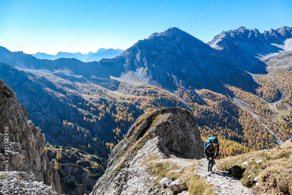 A woman with big hiking backpack walking on a pathway to reach the Grosse Gamswiesenspitze in Lienz Dolomites, Austria. Sharp slopes. Massive Alpine mountains. Solo wanderer, contemplating the nature