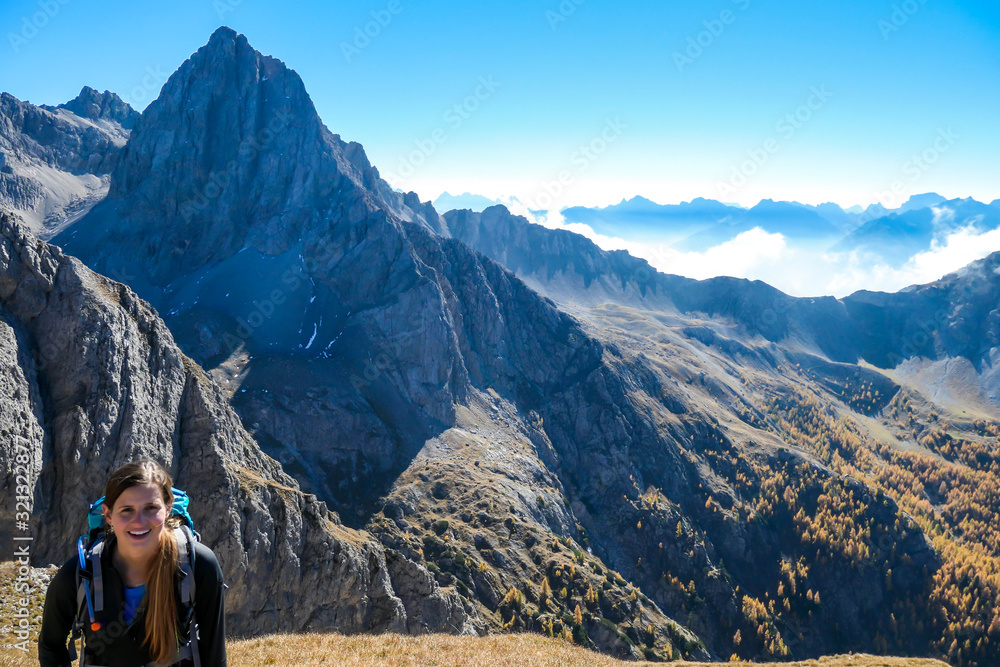Woman with big hiking backpack walking on a pathway to reach the Grosse Gamswiesenspitze in Lienz Dolomites, Austria. Sharp peaks in the back, and a valley covered with clouds. Massive Alpine mountain