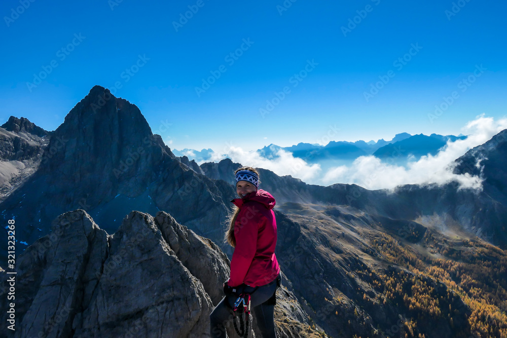 Woman in pink standing on the top of Grosse Gamswiesenspitze in Lienz Dolomites, Austria. Sharp, dangerous slopes. Massive Alpine mountains. Solo wanderer. She is happy and proud of her achievement