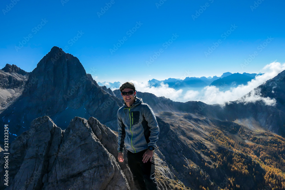 A man standing on the top of Grosse Gamswiesenspitze in Lienz Dolomites, Austria. Sharp, dangerous slopes. Massive Alpine mountains. Solo wanderer. He is happy and proud of his achievement. Freedom