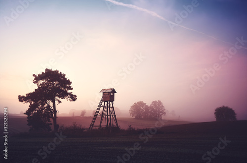 Rural landscape with silhouette of hunting tower on a field at sunrise.