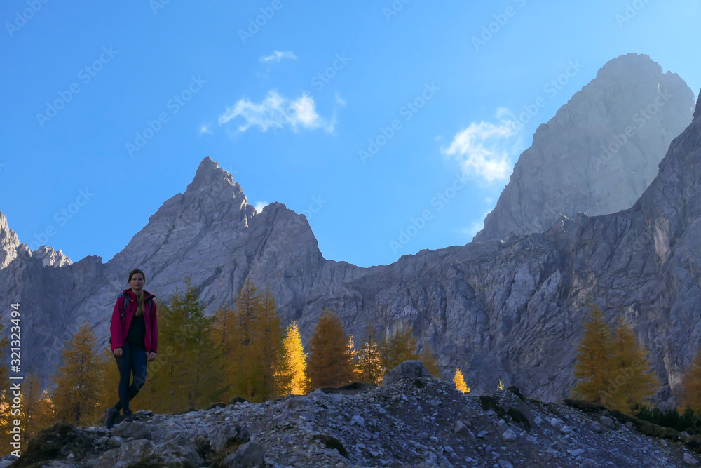 A woman standing next to a pathway, going to the top of Grosse Gamswiesenspitze in Lienz Dolomites, Austria. Sharp slopes. Massive Alpine mountains. Solo wanderer, contemplating the nature. New day