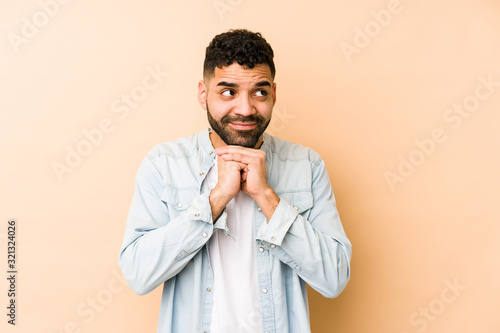 Young mixed race arabic man isolated keeps hands under chin, is looking happily aside.