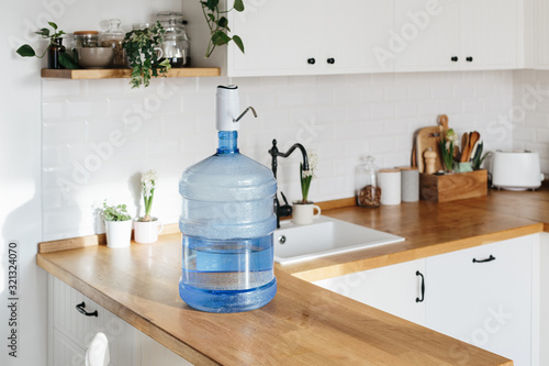 Cuadro en lienzo A larger bottle of clean water 19 liters with automatic white pomp in the interior of the apartment with a white kitchen in the background