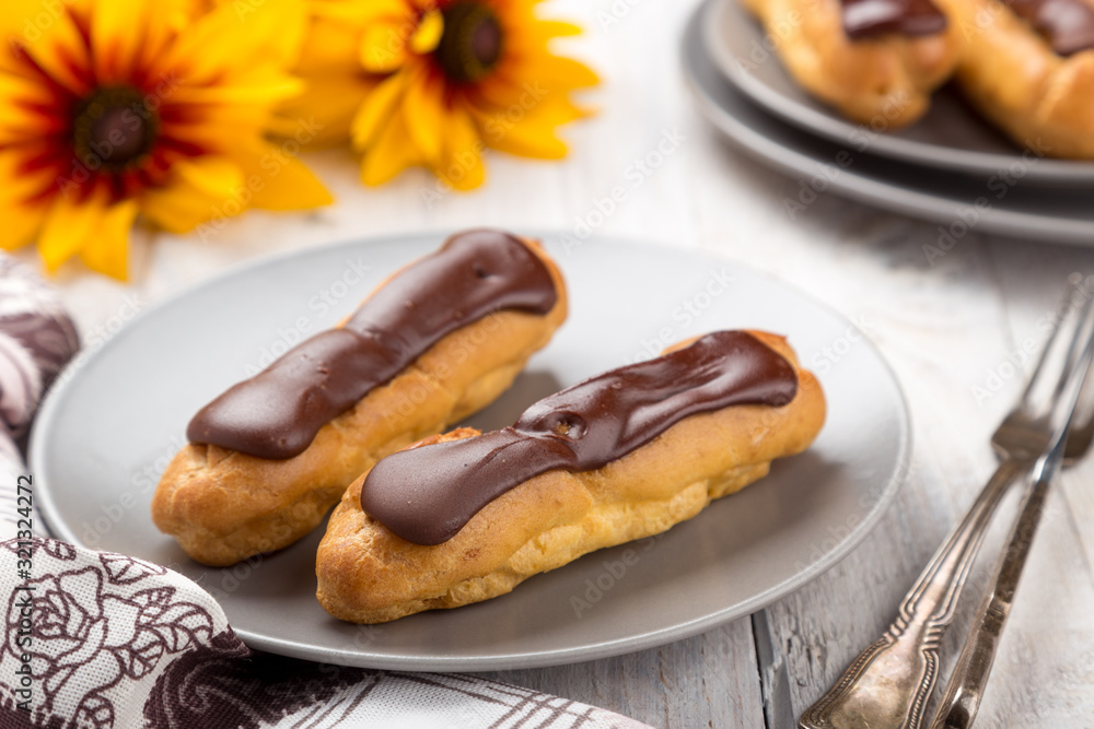 Tasty eclairs on a plate on a white wooden table. Served with flowers. Rectangular gray plate. Traditional french eclairs with chocolate. Home made cake eclairs. Traditional eclairs, profitroles class Tasty eclairs on a plate on a white wooden table. Served with flowers. Rectangular gray plate. Traditional french eclairs with chocolate. Home made cake eclairs. Traditional eclairs, profitroles class