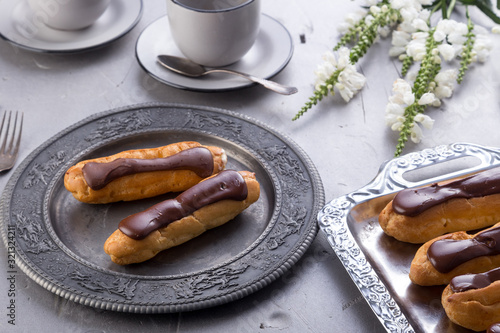 Tasty eclairs on a plate on a white wooden table. Served with flowers. Rectangular gray plate. Traditional french eclairs with chocolate. Home made cake eclairs. Traditional eclairs, profitroles class photo