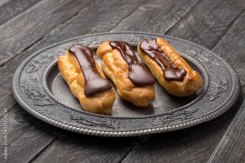 Tasty eclairs on a plate on a white wooden table. Served with flowers. Rectangular gray plate. Traditional french eclairs with chocolate. Home made cake eclairs. Traditional eclairs, profitroles class