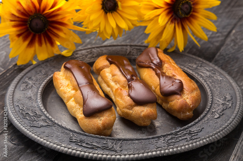 Tasty eclairs on a plate on a white wooden table. Served with flowers. Rectangular gray plate. Traditional french eclairs with chocolate. Home made cake eclairs. Traditional eclairs, profitroles class photo