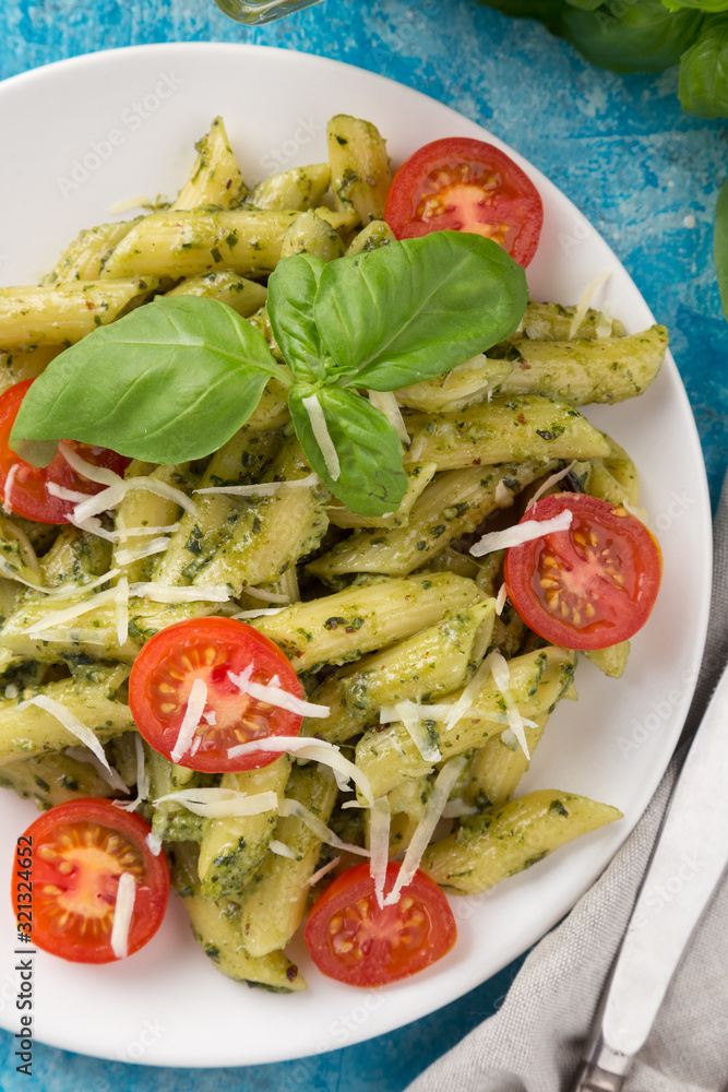 Pasta pesto with tomatoes on a blue table. Served with tomatoes, basil, olive oil, pesto, napkin, knife, fork. View from above. Top view. close-up photo Pasta pesto with tomatoes on a blue table. Served with tomatoes, basil, olive oil, pesto, napkin, knife, fork. View from above. Top view. close-up photo