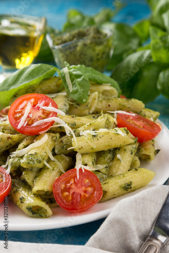 Pasta pesto with tomatoes on a blue table. Served with tomatoes, basil, olive oil, pesto, napkin, knife, fork. View from above. Top view. close-up photo