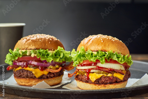 Two hamburgers and paper cup of drink on dark background
