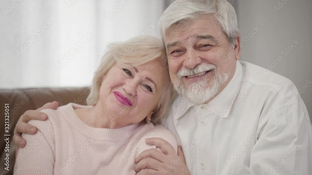 Portrait of smiling elderly Caucasian spouses looking at camera. Joyful mature husband and wife posing indoors. Happiness, love, lifestyle. Portrait of smiling elderly Caucasian spouses looking at camera. Joyful mature husband and wife posing indoors. Happiness, love, lifestyle.