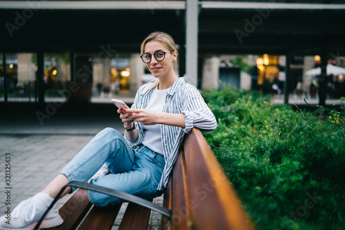 Smiling woman sitting on street bench with smartphone