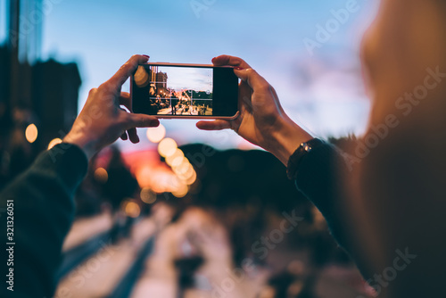 Selective focus on modern cellular phone using for clicking pictures via camera, millennial woman tourist taking photos or shooting video via mobile phone during evening walk for exploring new city