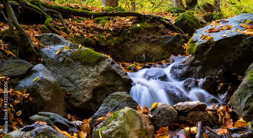 Little waterfall in the forest with leaves in autumn. long exposure.