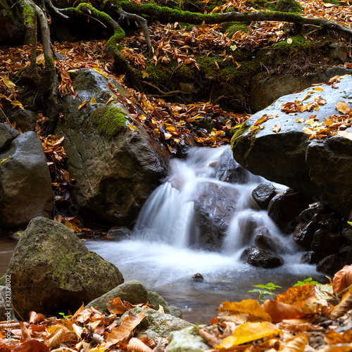 Little waterfall in the forest with leaves in autumn. long exposure.