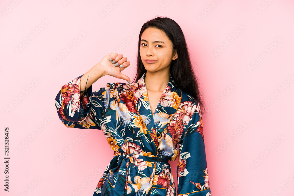 Young chinese woman wearing a asiatic pijama isolated showing a copy space on a palm and holding another hand on waist.