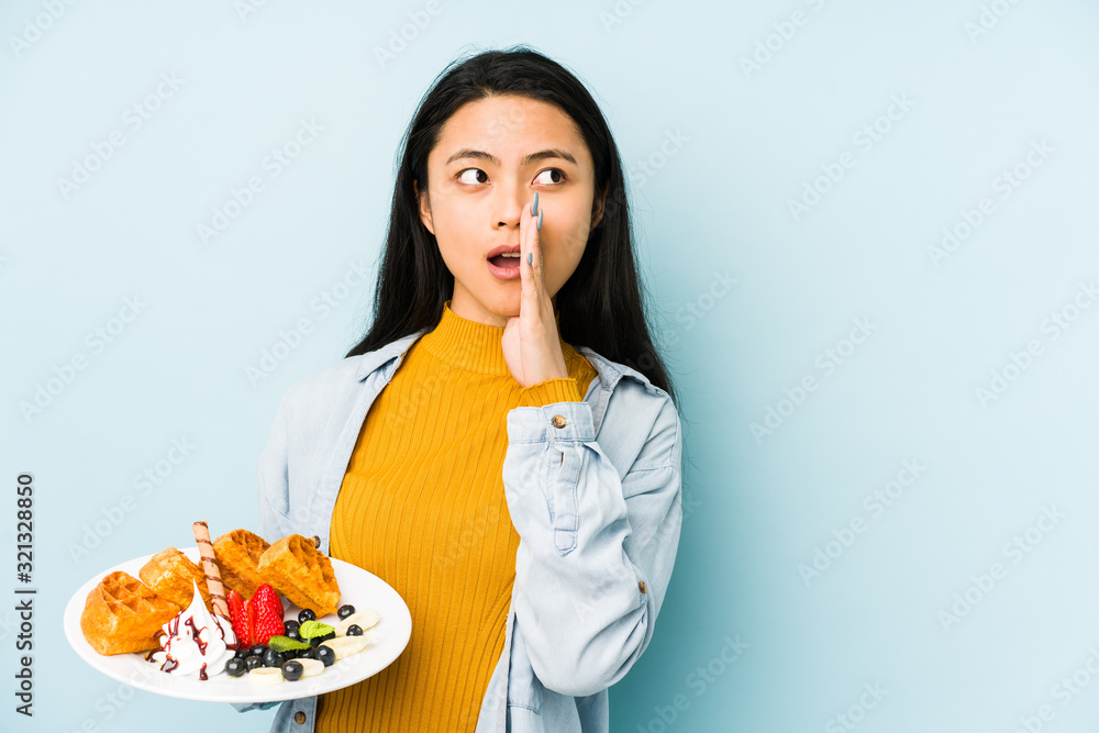 Young chinese woman holding waffle isolated on blue background pointing temple with finger, thinking, focused on a task. Young chinese woman holding waffle isolated on blue background pointing temple with finger, thinking, focused on a task.