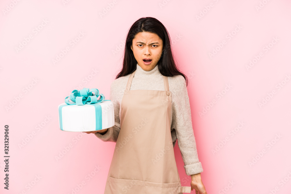Young chinese woman holding a cake isolated joyful and carefree showing a peace symbol with fingers. Young chinese woman holding a cake isolated joyful and carefree showing a peace symbol with fingers.