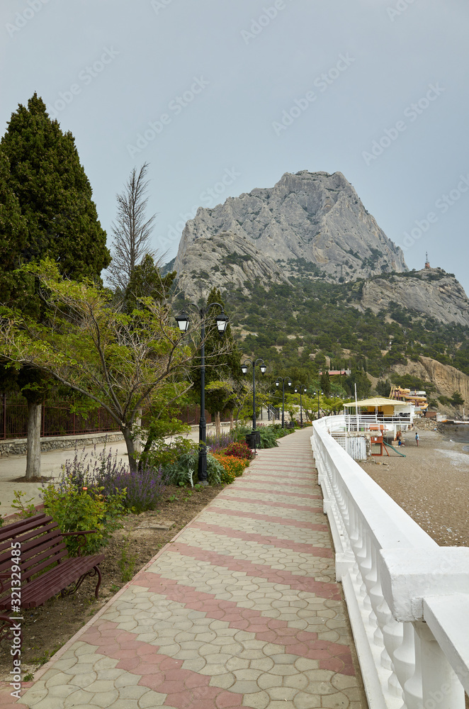 The coast of the Black Sea. Embankment alley for walks. View of Mount Sokol, low cloud cover. New World, Republic of Crimea
