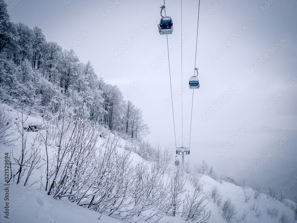 Obraz premium Winter Mountain landscape at the Rosa Khutor ski resort in Sochi, Russia. Cable car cabin over pine trees in the snow