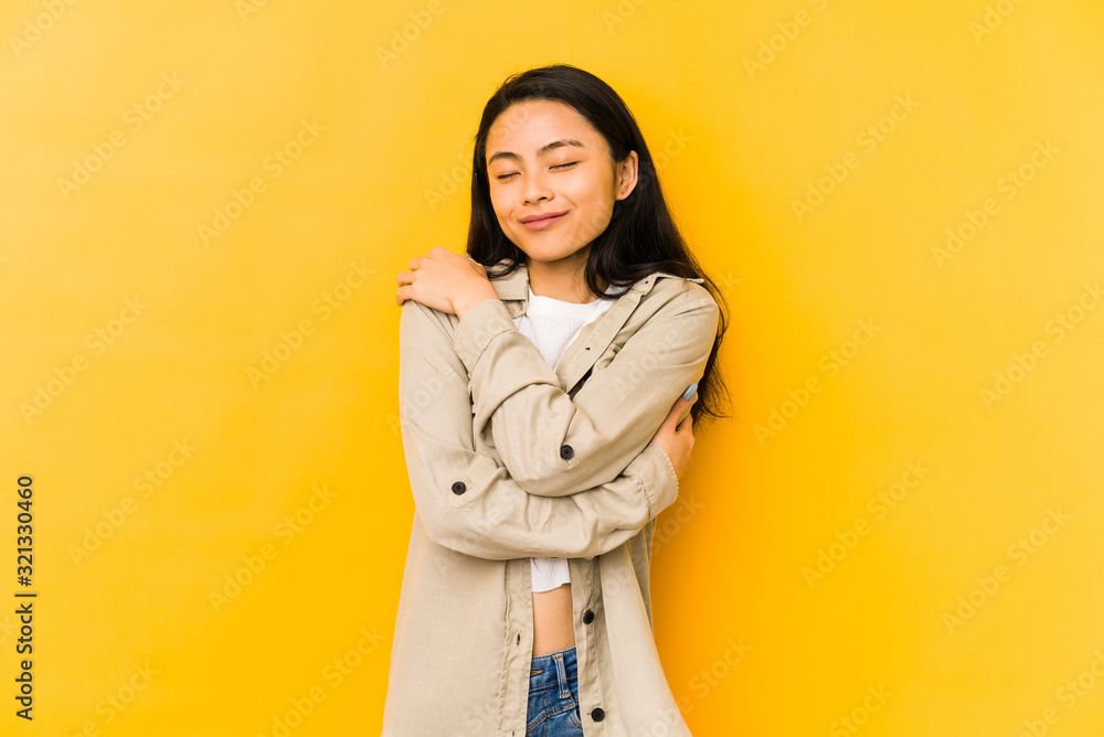Young chinese woman isolated on a yellow background hugs, smiling carefree and happy. Young chinese woman isolated on a yellow background hugs, smiling carefree and happy.